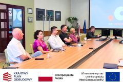 Spotkanie na sali konferencyjnej, po lewej siedzą uczestnicy spotkania, w tle widać ekran i prezentację.