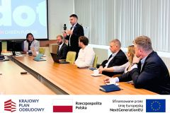Spotkanie na sali konferencyjnej, po prawej siedzą uczestnicy spotkania, w tle widać ekran i prezentację.