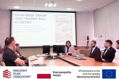 Spotkanie, przy stole siedzą uczestnicy po lewej i prawej stronie stołu, w tle ekran z prezentacją.