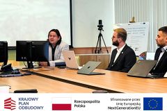 Trzech mężczyzn przy stole podczas spotkania, w tle ekran z prezentacją.