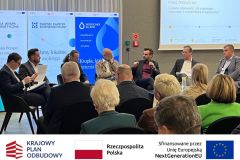 Panel dyskusyjny: siedmiu mężczyzn siedzi na scenie i przemawia. Po zdjęciem belka z logotypami KPO, flaga Polski oraz flaga Unii Europejskiej i napisem "Sfinansowano przez Unie Europejską".