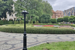 Słupek zraszający w park, w tle piękne kwiaty i krzewy, drzewa, fragmenty budynku i graffiti.