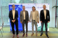 Zdjęcie grupowe z 4 osobami, są to mężczyźni, za nim stoją 3 rollup-y podświetlane ledowe, na nich logo Słupskich Wodociągów, Klastra SKB i projektu SWB.