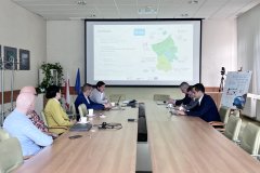 Sala konferencyjna, na środku stół, przy którym siedzą uczestnicy wizyty studyjnej, po lewej 5 osób, w tym jedna kobieta, po prawej 3 mężczyzn. W tle ekran z prezentacją.
