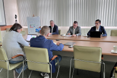 5 mężczyzn siedzi przy stole konferencyjnym. Dwóch z nich widzimy od tyłu, trzech pozostałych od przodu, prowadzą rozmowy.