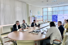 Sala konferencyjna, na środku stół, przy którym siedzą uczestnicy wizyty studyjnej, po lewej 3 mężczyzn, po prawej 4 mężczyzn i jedna kobieta, w tle sali 3 rollupy podświetlone z logo Słupskich Wodociągów oraz logo projektu SWB i Klastra.SKB
