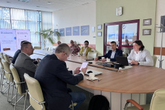 Sala konferencyjna, na środku stół, przy którym siedzą uczestnicy wizyty studyjnej, łącznie 8 osób, w tym jedna kobieta i 7 mężczyzn, rozmawiają.Sala konferencyjna, na środku stół, przy którym siedzą uczestnicy wizyty studyjnej, po lewej 5 osób, w tym jedna kobieta, po prawej 3 mężczyzn. W tle ekran z prezentacją. W tle widać rollupy.