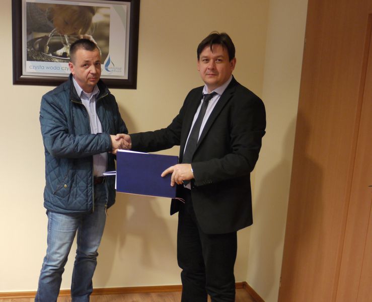 2 mężczyzn na zdjęciu, podają sobie ręce, jeden z nich trzyma umowę w dłoni.